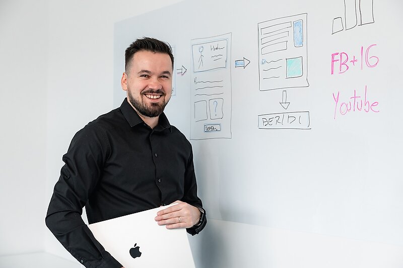 Ioan Drozd präsentiert lächelnd eine Content-Strategie mit Social-Media-Kanälen auf dem Whiteboard