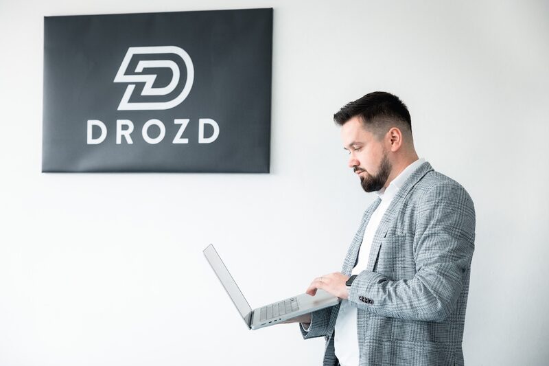 Ioan Drozd arbeitet am Laptop vor dem Firmenlogo an einer Marketing-Kampagne