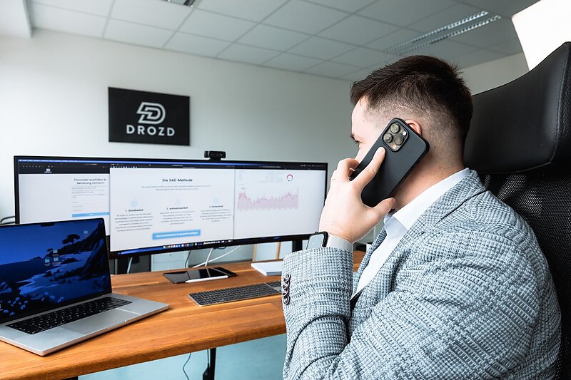 Ioan Drozd betreut Google Ads Kampagnen an zwei Bildschirmen und telefoniert dabei