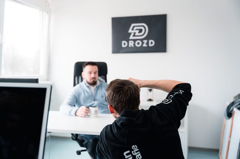 Ioan Drozd im Gespräch mit einem Bewerber im Büro, im Hintergrund das DROZD-Logo